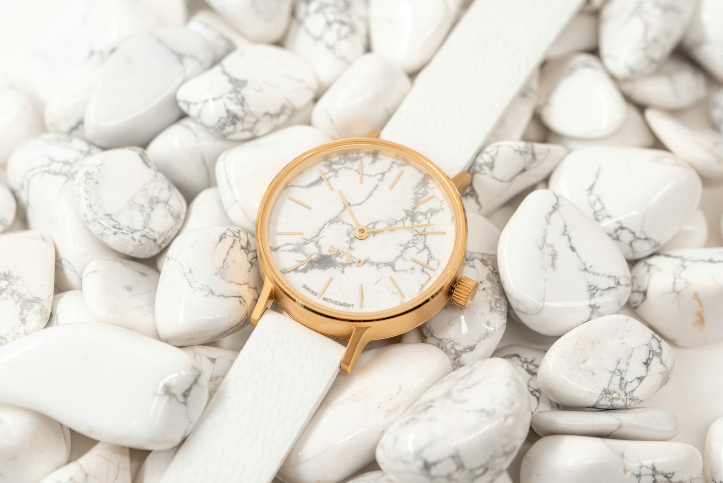 Un moderno orologio oro e bianco poggia su pietre marmorizzate.
