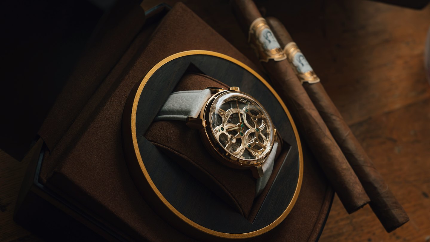 Orologio scheletro dorato e due sigari appoggiati sul legno.